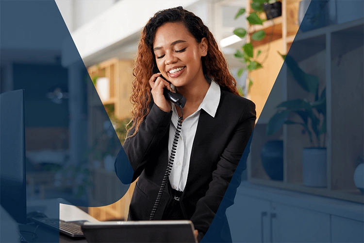 Businesswoman using a desk phone while working at a desk.
